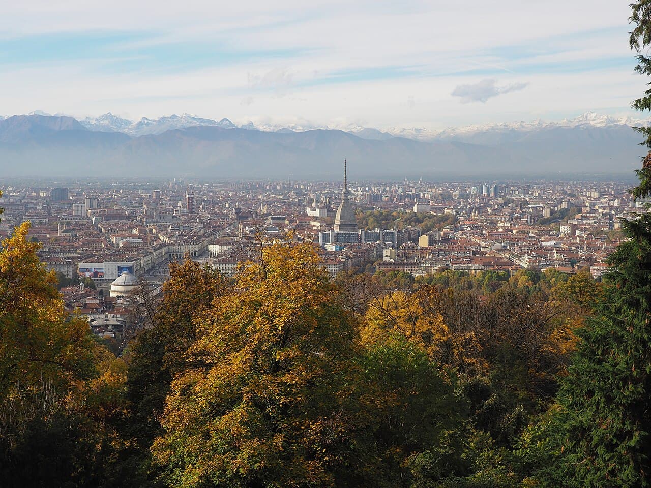 The city seen from the wooded hill in autumn, the Mole Antonelliana at its centre and the Alps beyond the rooftops
